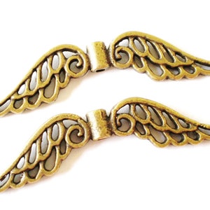 May include: Two gold-toned metal angel wings with a delicate, intricate design. The wings are connected by a small metal bar.