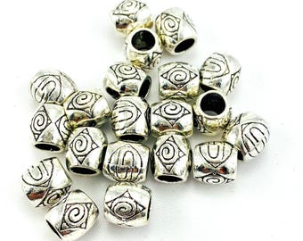 May include: A collection of small, barrel-shaped silver-toned metal beads. Each bead features a raised, embossed design consisting of a central spiral motif enclosed within a diamond-shaped border, with additional linear patterns on the sides.