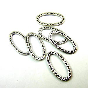 May include: A collection of five silver-toned metal oval links, each featuring a textured, hammered surface pattern along the outer edge. These open, hollow oval-shaped connectors are arranged in a scattered, overlapping formation.