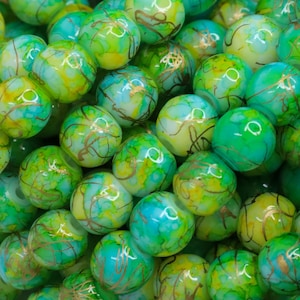 May include: Close-up of a pile of round beads in shades of green, teal, and yellow. The beads have a marbled effect with gold-colored veining throughout. The beads are likely used for jewelry making or crafts.