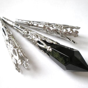 May include: Silver-toned metal jewelry findings with intricate filigree designs. A faceted black crystal pendant is featured, along with three decorative metal caps. The findings are displayed against a white background.