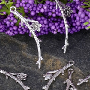 May include: Silver tone metal charms shaped like branches with small flower accents. The charms have a loop at the top for attaching to jewelry or other crafts.