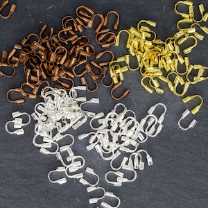 May include: An overhead shot displays a collection of jewelry findings in three metallic colors: silver, gold, and bronze. The findings are U-shaped with a rectangular base, suitable for jewelry making and crafting.