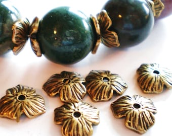 Può includere: Primo piano di sei cappucci per perline in metallo color oro a forma di fiore. I cappucci per perline hanno una superficie testurizzata e un piccolo foro al centro.