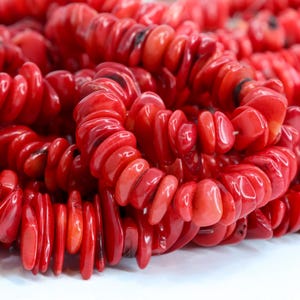 May include: Close-up of several strands of bright red coral beads. The beads are irregularly shaped and strung together, creating a textured and vibrant appearance. The coral has a glossy finish, reflecting light and adding to its visual appeal.
