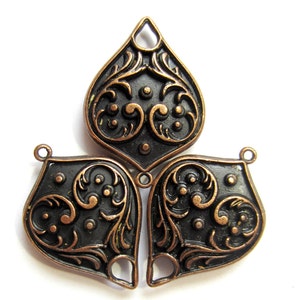 May include: A copper-colored metal pendant with a three-leaf design. Each leaf has a black background with intricate copper-colored swirls and dots.