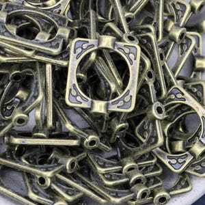 K&ouml;nnte beinhalten: Ein Haufen antiker, bronzefarbener Metallbeschlagteile. Jedes Teil hat einen rechteckigen Rahmen mit einem zentralen Kreis und dekorativen bl&uuml;tenartigen Mustern. Die Beschl&auml;ge haben eine Vintage-&Auml;sthetik, geeignet f&uuml;r Bastel- oder Restaurierungsprojekte.