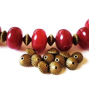 May include: A strand of red beads with gold-toned metal bead caps. The beads are round and have a glossy finish. There are 12 gold-toned metal bead caps.