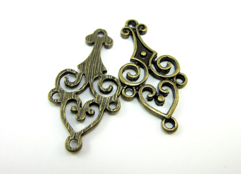 May include: Two antique gold metal filigree charms with intricate swirl designs. The charms have a textured finish and are perfect for adding a vintage touch to jewelry or crafts.