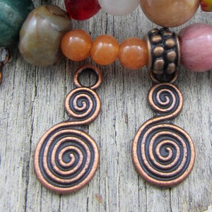 May include: Two copper spiral charms with a loop at the top. The charms are a double spiral design with a smaller spiral on top of a larger spiral.