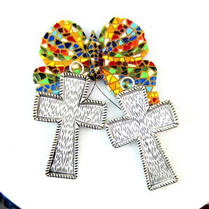 May include: Two silver-colored cross pendants with textured detailing, connected to a colorful mosaic butterfly. The butterfly wings feature a vibrant array of colors including red, yellow, blue, and green. The pendants have a loop for hanging.
