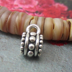 Puede incluir: Tapón de cuentas de metal plateado con un diseño decorativo. El tapón de cuentas tiene un bucle en la parte superior para sujetarlo a un collar o pulsera.