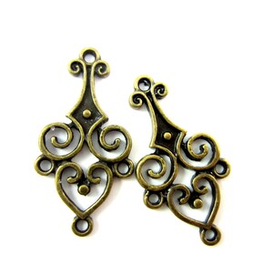 May include: Two antique gold-toned metal charms with intricate scrollwork and heart designs. The charms have a loop at the top for attaching to jewelry or other crafts.
