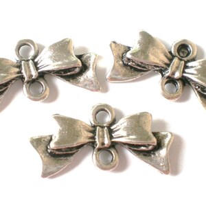 May include: Three silver-toned metal bow charms with two holes each. The bows are detailed with a textured surface and have a three-dimensional appearance.