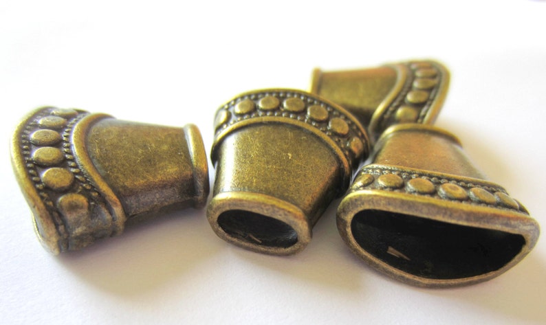 Puede incluir: Cuatro tapones de extremo de metal de color dorado antiguo con un ribete de cuentas decorativas. Los tapones de extremo tienen forma de peque&ntilde;as campanas.