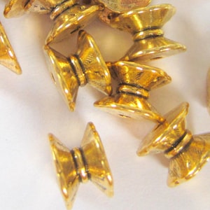 May include: A group of gold-colored metal beads with a decorative design. The beads have a raised center and a fluted edge.