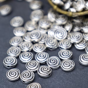 May include: A close-up of a pile of silver metal beads with a spiral design. The beads are scattered on a dark gray surface.