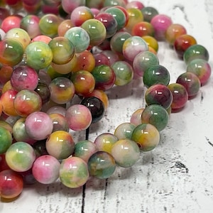 May include: A strand of colourful jade beads with a mix of green, pink, yellow, and white tones. The beads are round and smooth, and they are strung together on a clear thread.