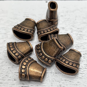 May include: A group of eight antique gold-toned metal cord ends with a decorative beaded trim. The cord ends are shaped like a cone with a rounded top and a flat bottom.