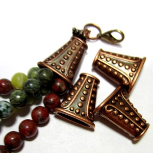 May include: Four copper-toned metal bead caps with a textured, dotted design. The caps are cone-shaped and have a decorative, scalloped edge. The caps are arranged in a cluster on a white background.