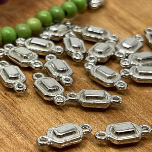 May include: A group of silver-toned metal connector charms with a rectangular shape and two loops on each side. The charms have a slightly raised, beveled edge.