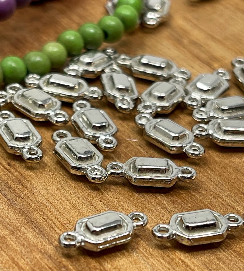 May include: A group of silver-toned metal connector charms with a rectangular shape and two loops on each side. The charms have a slightly raised, beveled edge.