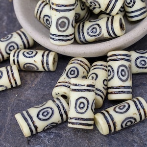 May include: A collection of white bone beads with black circular patterns. The beads are cylindrical and have a smooth, polished finish.