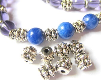 Può includere: Primo piano di un braccialetto di perline con perline blu e viola e dettagli in metallo color argento. Diverse perline in metallo color argento sciolte sono sparse nelle vicinanze. Le perline sono rotonde e lisce, con una finitura lucida.