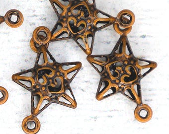 Könnte beinhalten: Eine Sammlung von sternförmigen Anhängern aus bronzefarbenem Metall, die jeweils ein kompliziertes durchbrochenes Design mit einem zentralen Om-Symbol aufweisen. Diese Schmuckkomponenten haben ein dunkles, antikes Finish und kleine Ösen.
