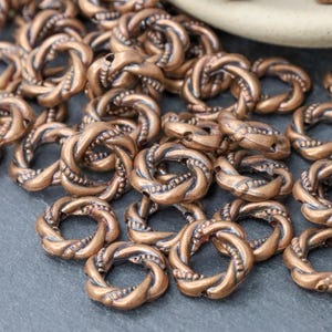 May include: A pile of copper-colored metal beads with a twisted rope design. The beads are small and have a hole in the center for stringing.