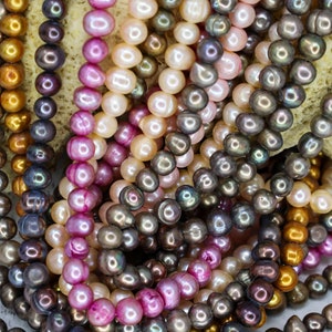 Peut inclure: Gros plan sur un assortiment de fils de perles de différentes couleurs, dont le rose, le blanc, l'or et le noir. Les perles sont disposées en tas, révélant leur éclat iridescent.