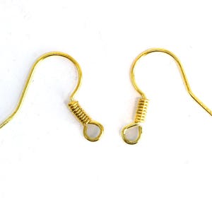 May include: Two gold-colored earring hooks on a white background. Each hook has a curved wire design with a coiled spring detail and a small loop at the bottom. The hooks are designed for jewelry making.