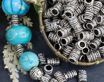 May include: A collection of cylindrical silver-toned metal beads featuring intricate etched geometric patterns, alongside a strand of round turquoise-colored beads with smooth and marbled textures separated by smaller silver-toned spacer beads.