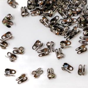 May include: A pile of silver metal clasps with a ball on one end and two loops on the other. The clasps are scattered on a white surface.