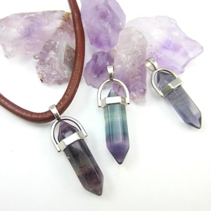 May include: A brown leather necklace with three silver and crystal pendants. Each pendant features a pointed crystal with a silver setting. The crystals are a mix of green, blue, and purple.