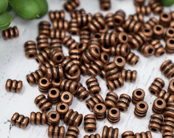 Può includere: Un grande mucchio di perline color rame con strisce nere. Le perline sono piccole e rotonde, e sono perfette per la creazione di gioielli.