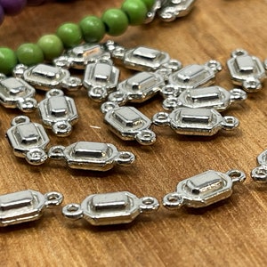 May include: Silver-toned metal connector charms with a rectangular shape and two loops on each side. The charms are scattered on a wooden surface.