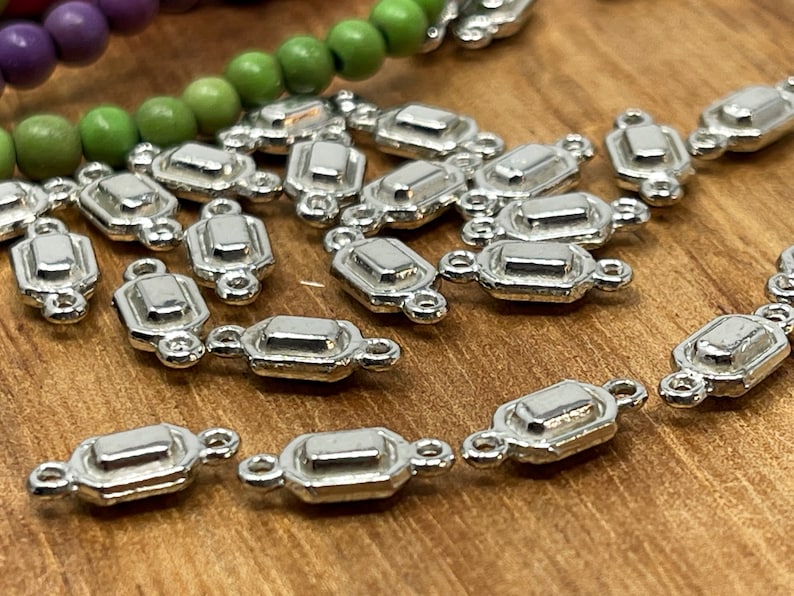 May include: Silver-toned metal connector charms with a rectangular shape and two loops on each side. The charms are scattered on a wooden surface.