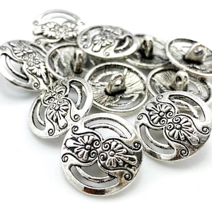 May include: A collection of silver-colored metal buttons with an antique finish. Each button features a floral design with openwork details. The buttons have a shank on the back for sewing onto fabric. Ideal for sewing projects.