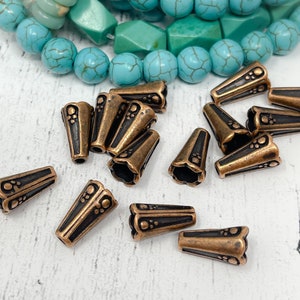 May include: A collection of 14 antique copper-toned metal cone-shaped bead caps with a decorative design. The caps have a black finish and are scattered on a white surface.