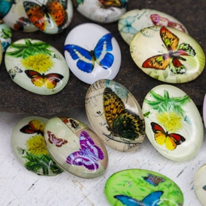 May include: Assortment of oval-shaped glass cabochons with butterfly designs. The cabochons feature various butterflies with different colors and patterns, including blue, purple, green, yellow, and red butterflies.