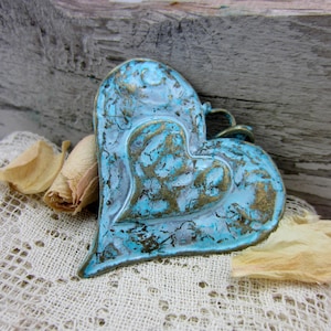 May include: A turquoise blue heart-shaped metal pendant with a distressed finish. The pendant has a raised heart design and is made of metal with a rustic look.