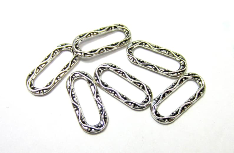 May include: Six silver oval-shaped metal rings with a decorative, ornate design. The rings are all the same size and have a smooth, polished finish.