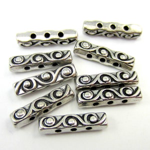 May include: Silver metal spacer beads with a decorative swirl pattern and three holes. The beads are approximately 1 inch long.
