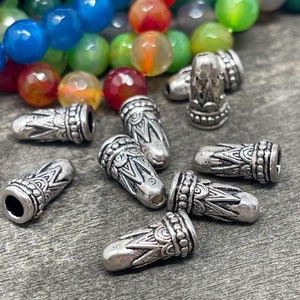 May include: Silver metal bead caps with a decorative design. The caps are about 1 inch long and have a hole in the center for stringing.