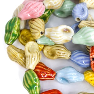 May include: A collection of colorful ceramic beads in various shapes and hues. The beads are in shades of pink, green, yellow, blue, and red. The beads are strung together, suggesting they are for jewelry making or crafting.