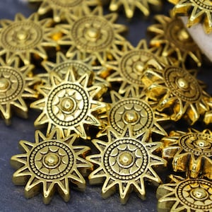 May include: A group of gold-toned metal star-shaped beads with a raised circular design in the center. The beads have a slightly textured finish.