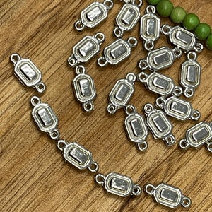 May include: A group of silver-toned metal connector charms with a rectangular shape and two loops on each side. The charms have a slightly raised, textured design.