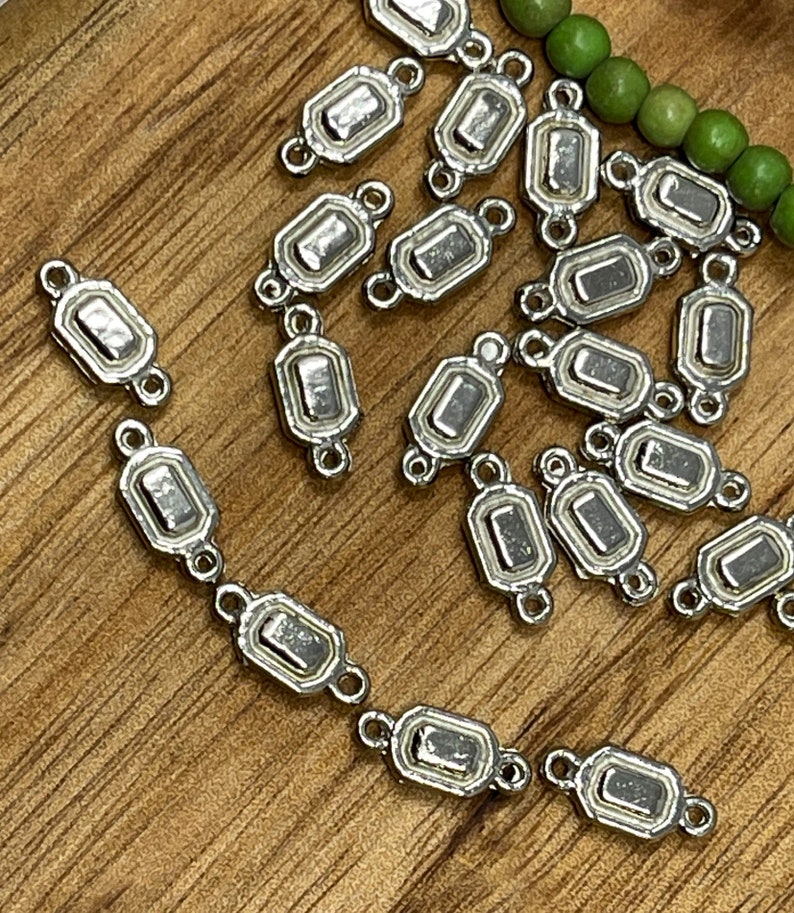 May include: A group of silver-toned metal connector charms with a rectangular shape and two loops on each side. The charms have a slightly raised, textured design.