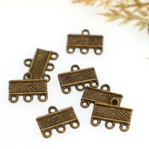 May include: A collection of antique bronze-toned metal jewelry connectors. Each rectangular piece features a textured, wavy line pattern across the front surface and includes three small circular loops along the bottom edge for attaching jewelry components.